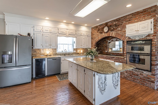 kitchen with stainless steel appliances, a kitchen island, brick wall, light stone countertops, and white cabinets