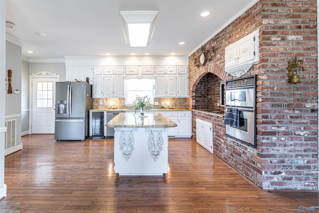 kitchen featuring appliances with stainless steel finishes, white cabinets, backsplash, a center island, and light stone countertops