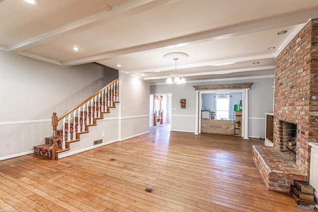 unfurnished living room featuring beamed ceiling, wood-type flooring, a brick fireplace, and a chandelier