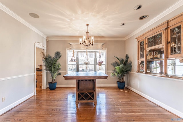 dining room with wood-type flooring, ornamental molding, and an inviting chandelier