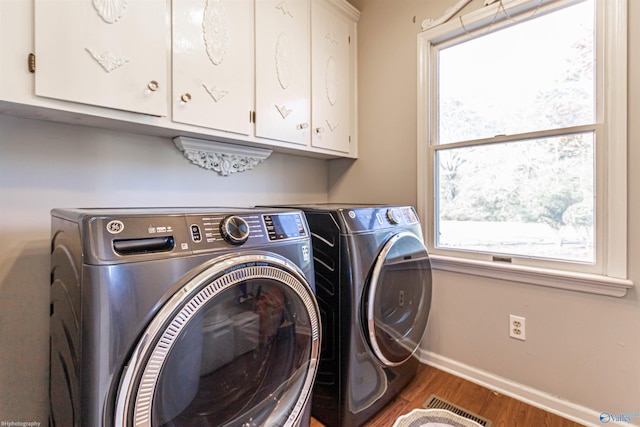 laundry room featuring cabinets, a healthy amount of sunlight, dark hardwood / wood-style flooring, and washing machine and dryer