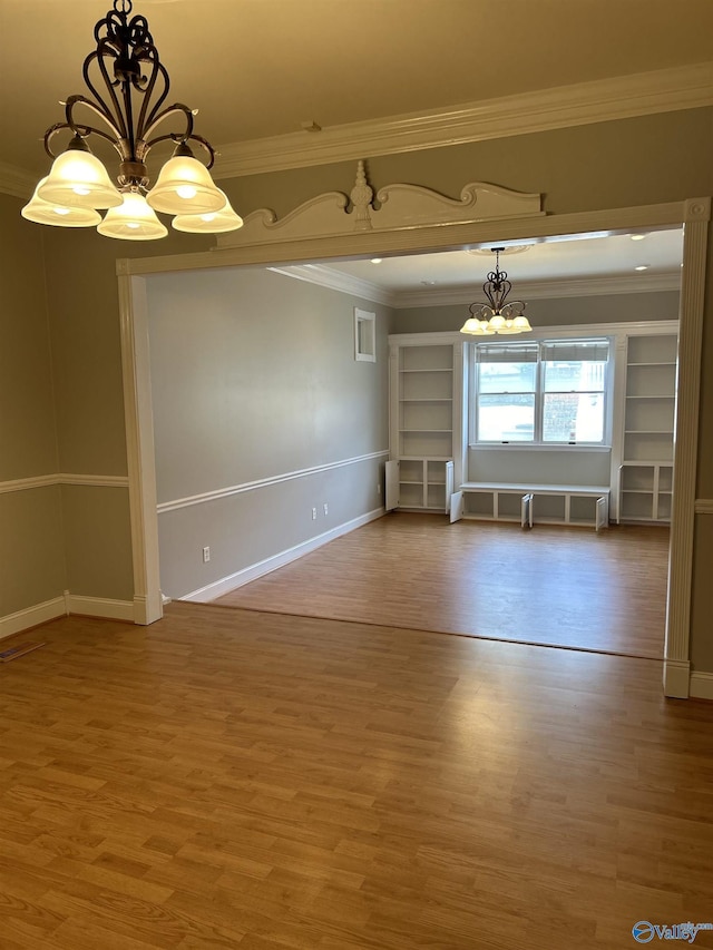 spare room featuring ornamental molding, wood-type flooring, and an inviting chandelier