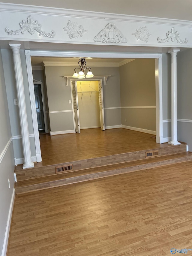 unfurnished living room featuring crown molding, wood-type flooring, and ornate columns