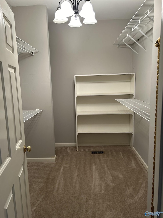 spacious closet with dark carpet and a chandelier