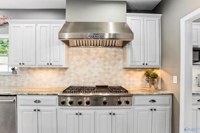 kitchen with appliances with stainless steel finishes, light stone countertops, wall chimney range hood, and white cabinets