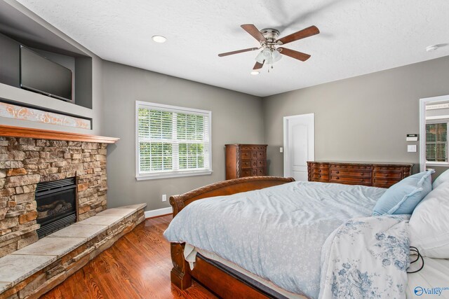 bedroom with ceiling fan, dark wood-type flooring, and a stone fireplace