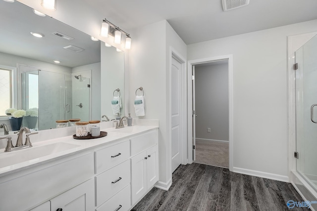 bathroom with a shower with shower door, hardwood / wood-style floors, and dual bowl vanity