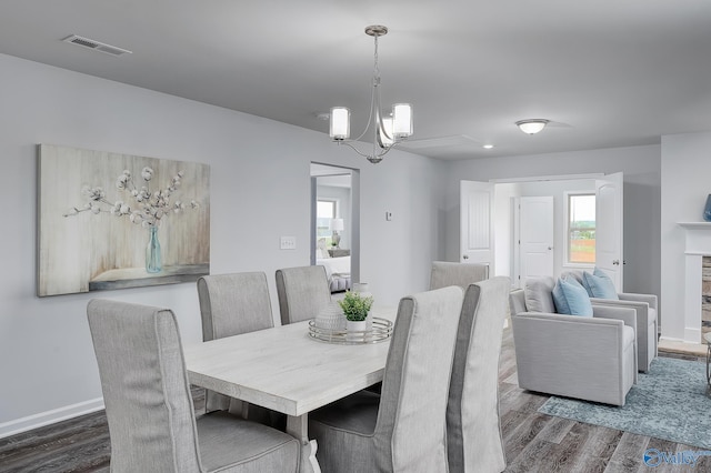 dining space with baseboards, visible vents, a fireplace with raised hearth, dark wood-style floors, and a notable chandelier