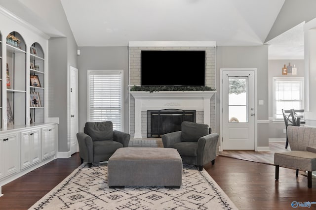 living room with wood-type flooring, a wealth of natural light, vaulted ceiling, and a brick fireplace