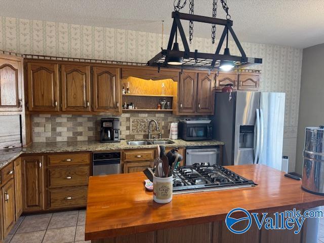 kitchen featuring stainless steel appliances, butcher block counters, a sink, a textured ceiling, and wallpapered walls