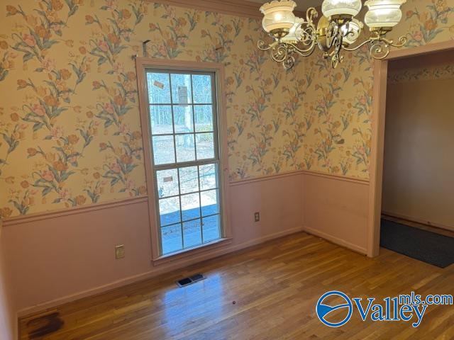 spare room with wood finished floors, a wainscoted wall, a notable chandelier, and wallpapered walls