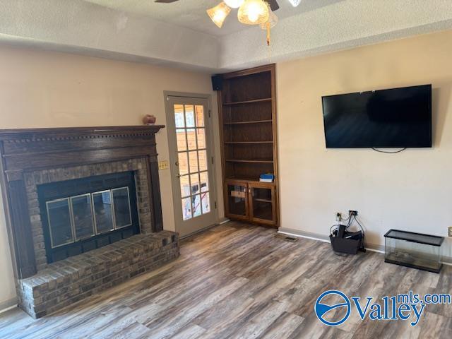 unfurnished living room featuring a ceiling fan, a fireplace, baseboards, and wood finished floors