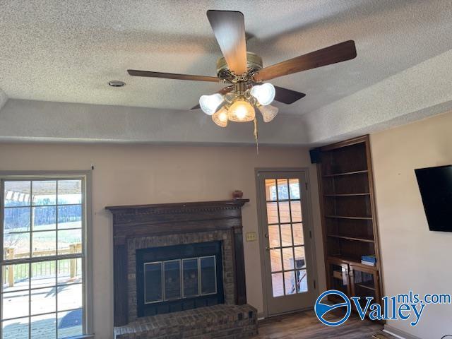 living area featuring a textured ceiling, a fireplace, wood finished floors, and a healthy amount of sunlight