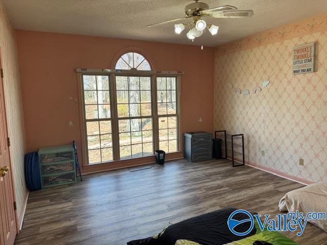 interior space with wallpapered walls, a ceiling fan, a textured ceiling, and wood finished floors