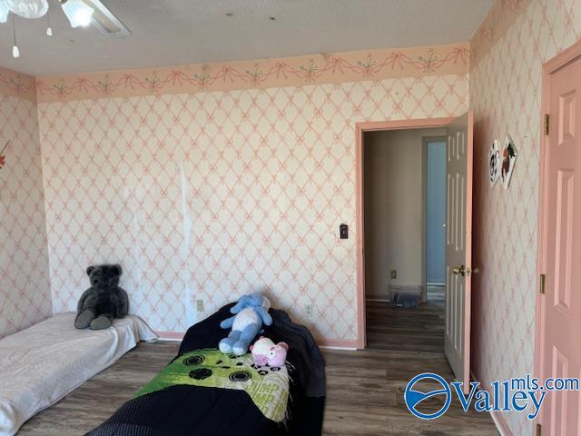 bedroom featuring wood finished floors, ceiling fan, baseboards, and wallpapered walls