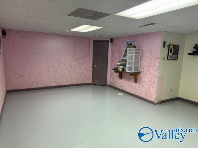 spare room featuring wallpapered walls, a drop ceiling, and baseboards