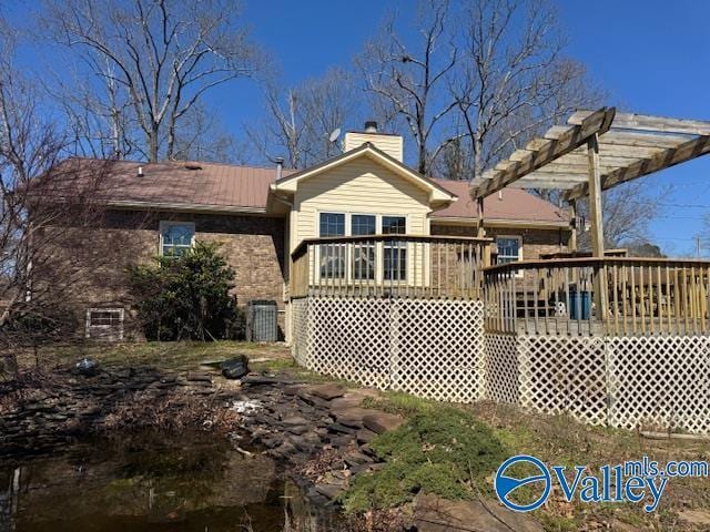 back of property with a chimney, a pergola, and a wooden deck