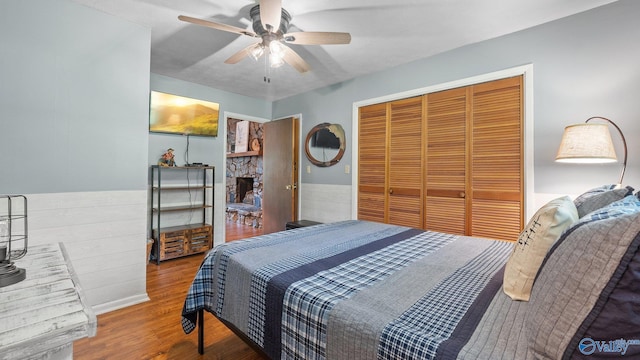 bedroom featuring a fireplace, ceiling fan, a closet, and wood finished floors