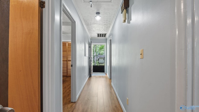 hall featuring ornamental molding, baseboards, visible vents, and wood finished floors