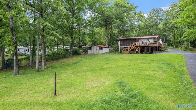 view of yard featuring driveway, an outdoor structure, stairs, a wooden deck, and a storage shed