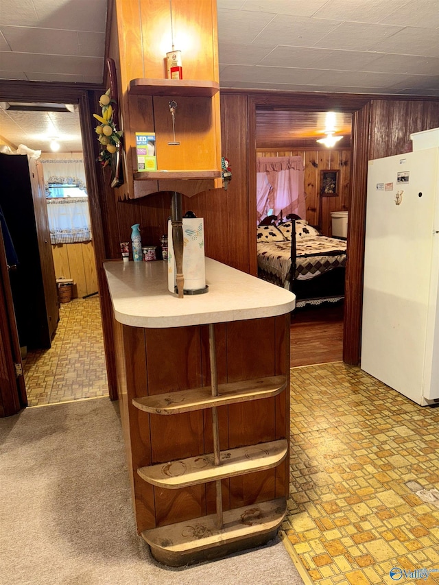 kitchen with wooden walls, light countertops, freestanding refrigerator, brown cabinets, and open shelves