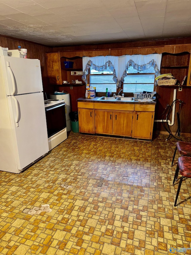 kitchen featuring white appliances, wood walls, a sink, and brown cabinetry