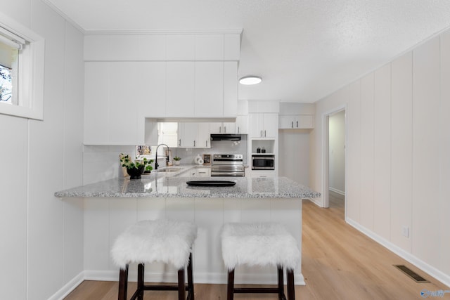 kitchen with stainless steel appliances, white cabinetry, light stone countertops, and kitchen peninsula