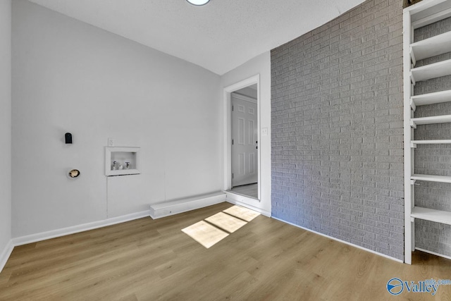 laundry room with hardwood / wood-style flooring, brick wall, hookup for an electric dryer, and hookup for a washing machine