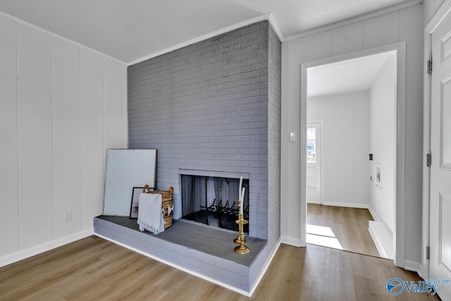 living room featuring hardwood / wood-style flooring, a brick fireplace, a textured ceiling, and crown molding