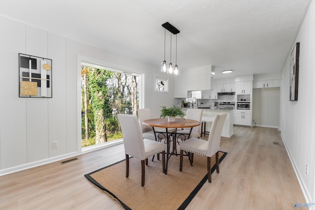 dining area featuring sink, a textured ceiling, and light wood-type flooring