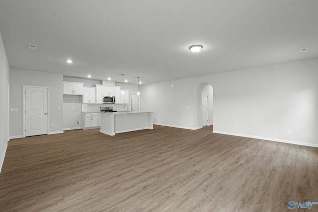 unfurnished living room featuring recessed lighting, light wood-style flooring, baseboards, and arched walkways