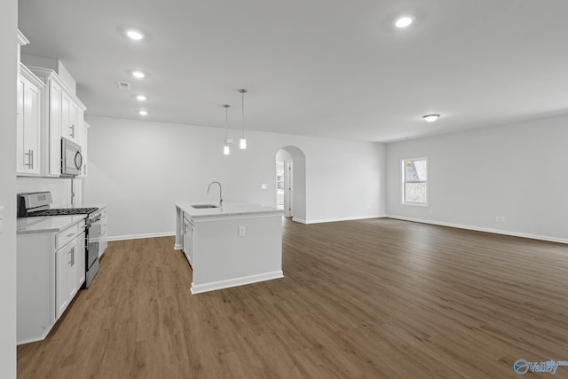kitchen with a sink, stainless steel appliances, arched walkways, white cabinets, and wood finished floors