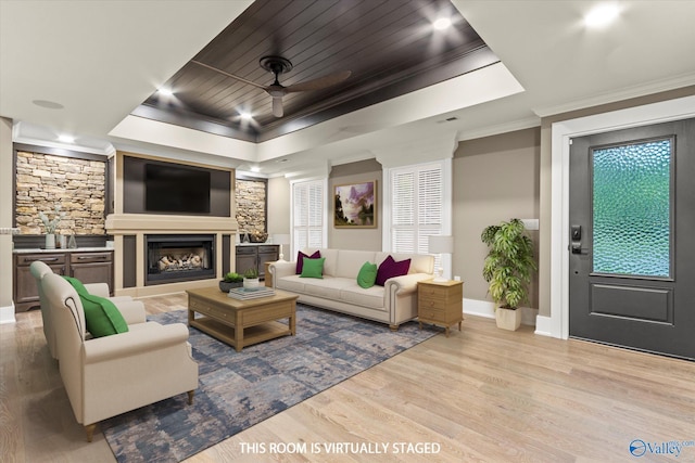 living room with wood ceiling, ceiling fan, a tray ceiling, ornamental molding, and light wood-type flooring