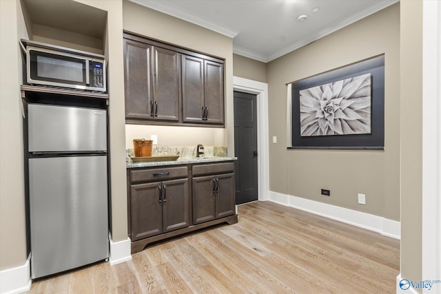 kitchen with sink, appliances with stainless steel finishes, dark brown cabinets, ornamental molding, and light wood-type flooring