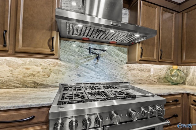 kitchen featuring light stone counters, wall chimney exhaust hood, decorative backsplash, and stainless steel gas range oven