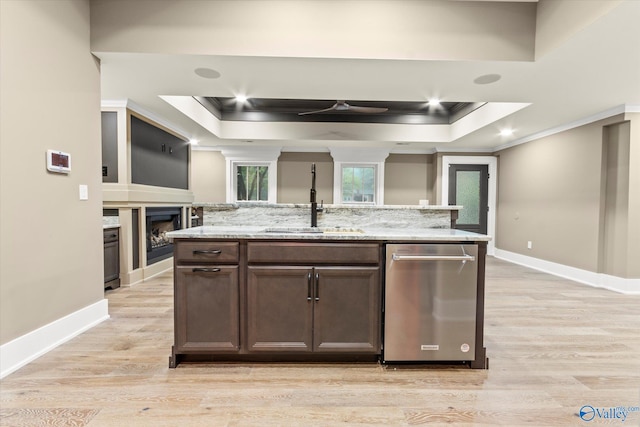 kitchen featuring a raised ceiling, sink, a center island with sink, and light stone counters