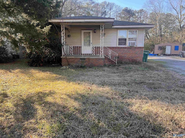 bungalow-style house featuring a front yard, covered porch, and a storage unit