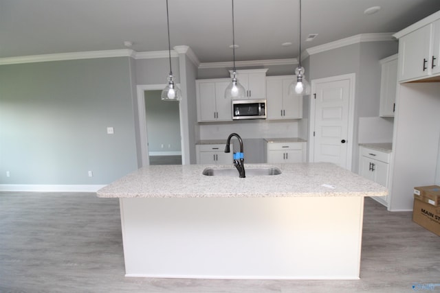 kitchen featuring pendant lighting, sink, white cabinetry, light stone countertops, and a center island with sink