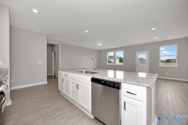 kitchen with a wealth of natural light, stainless steel dishwasher, a center island with sink, and white cabinets