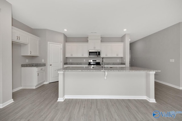 kitchen with a kitchen island with sink, light hardwood / wood-style flooring, stainless steel appliances, white cabinets, and light stone counters