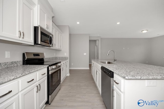 kitchen with white cabinets, a center island with sink, appliances with stainless steel finishes, light hardwood / wood-style flooring, and sink