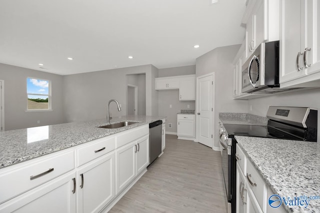 kitchen with sink, stainless steel appliances, white cabinets, light stone counters, and light hardwood / wood-style flooring