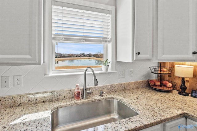 kitchen with tasteful backsplash, white cabinetry, and a sink