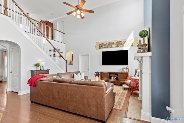 living room featuring ceiling fan, stairs, arched walkways, and wood finished floors