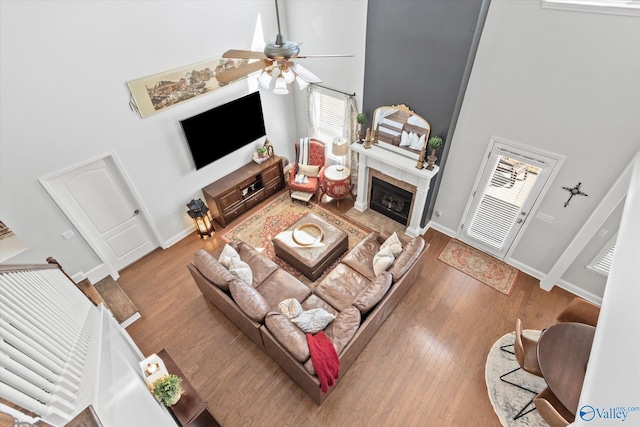 living area with a towering ceiling, a tiled fireplace, a ceiling fan, wood finished floors, and baseboards