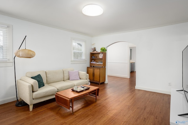 living area featuring baseboards, arched walkways, wood finished floors, and ornamental molding