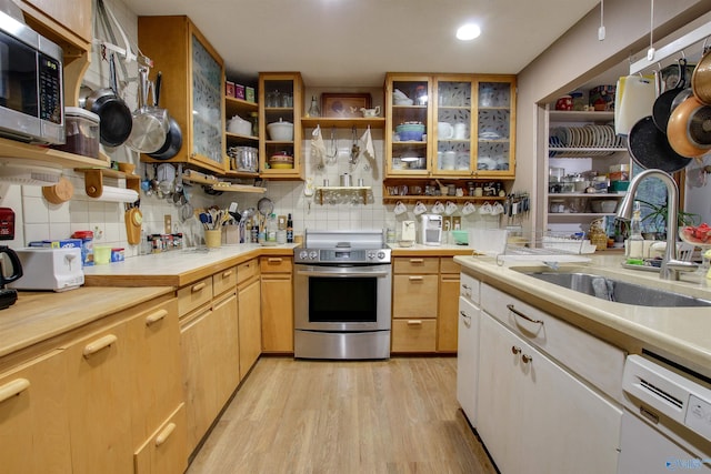 kitchen with stainless steel appliances, tasteful backsplash, sink, and light wood-type flooring