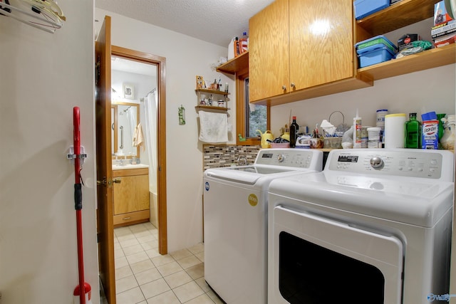 washroom with cabinets, a textured ceiling, washer and clothes dryer, and light tile patterned floors