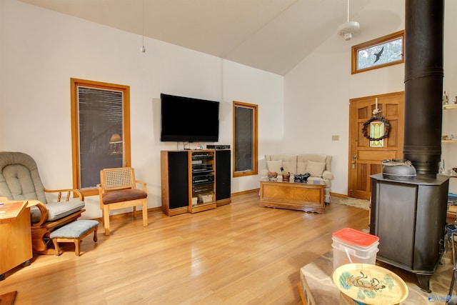 living room with high vaulted ceiling, a wood stove, and light wood-type flooring