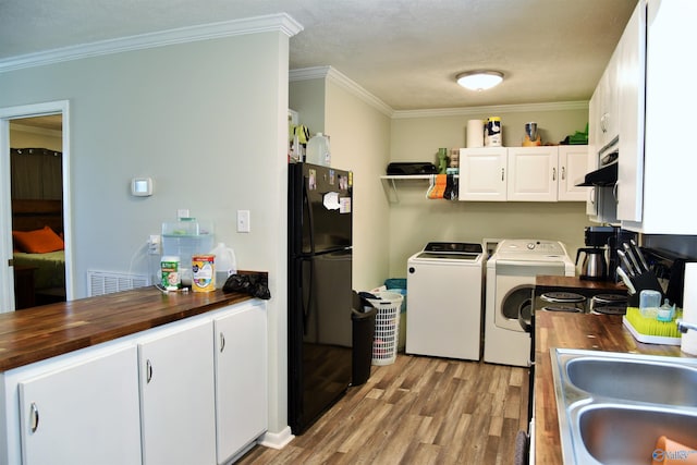 clothes washing area with washing machine and clothes dryer, laundry area, a sink, crown molding, and light wood-type flooring